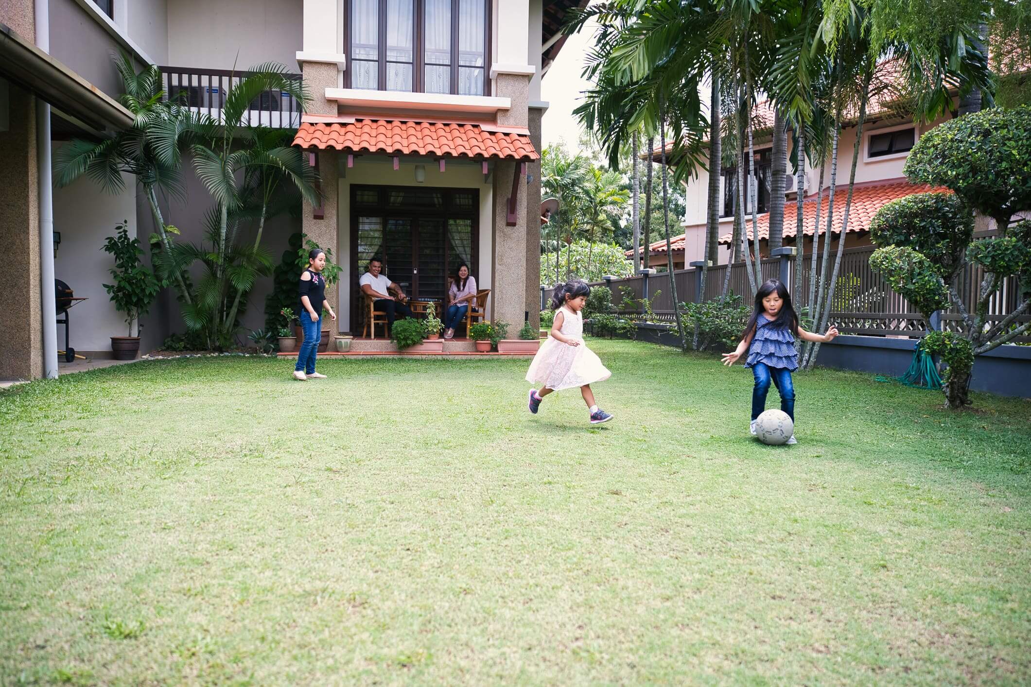 Children playing with a ball on a grassy lawn near a house.