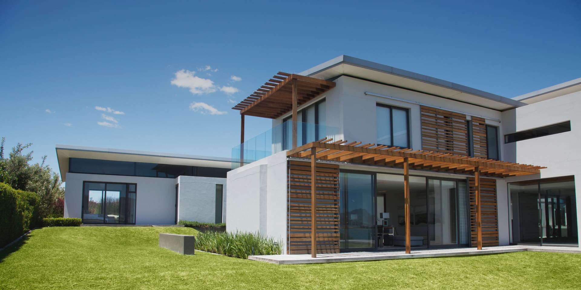 Modern two story house with wooden pergola and large windows.