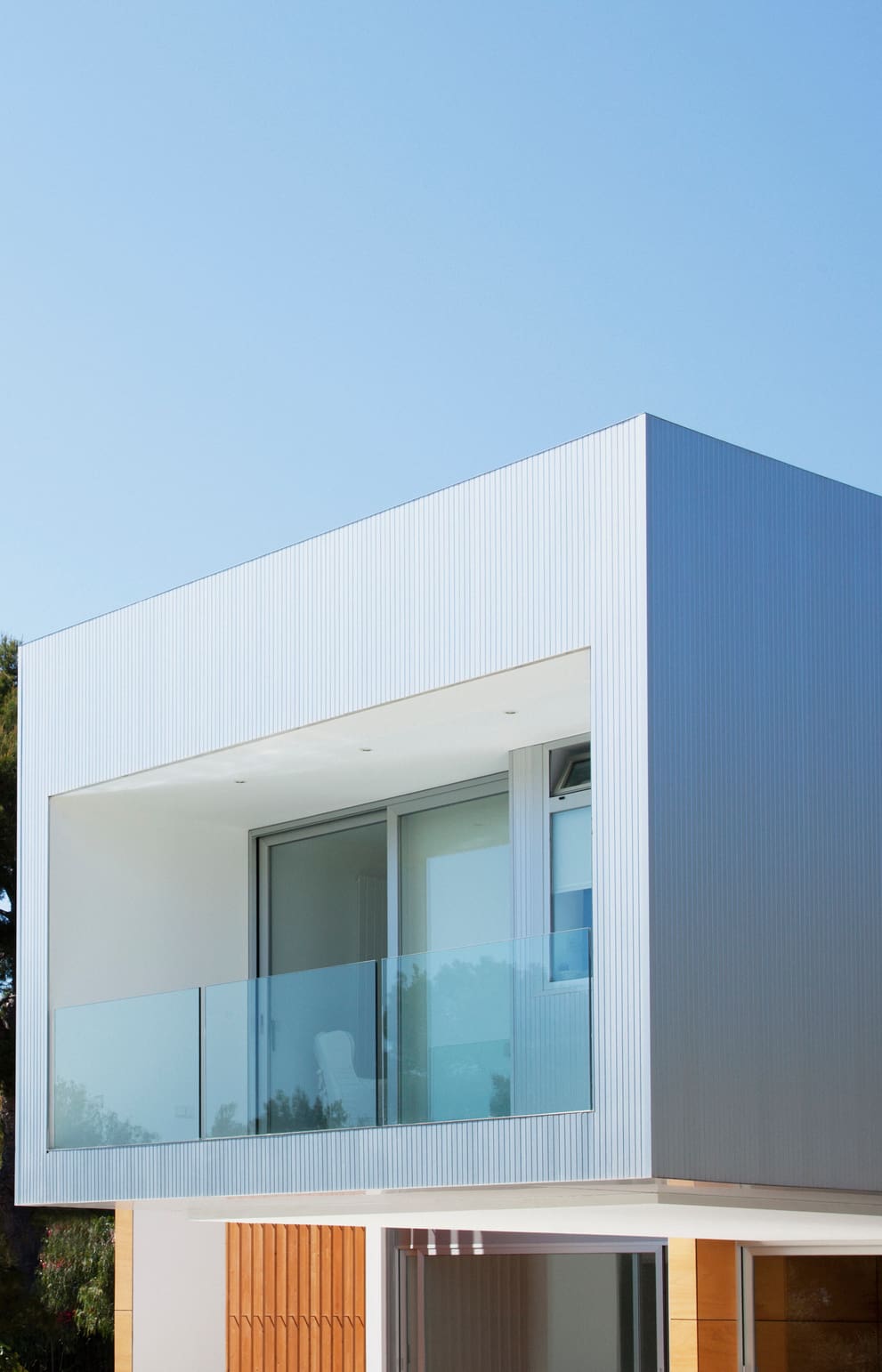 Modern white building with glass balcony under clear blue sky.