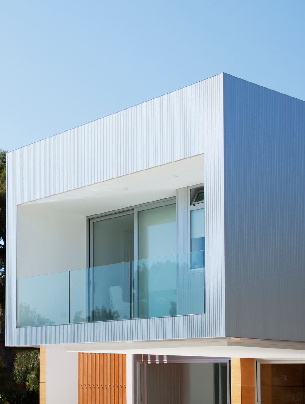 Modern white building with glass balcony and large windows.
