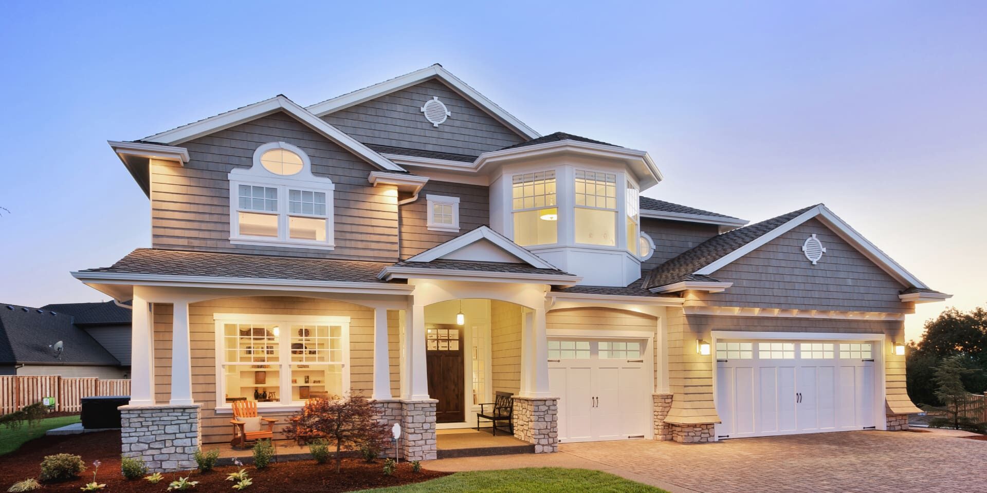 A modern two story house with warm exterior lighting at dusk.